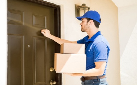 Closeup of a young man delivering a few packages to a house and knocking on its door